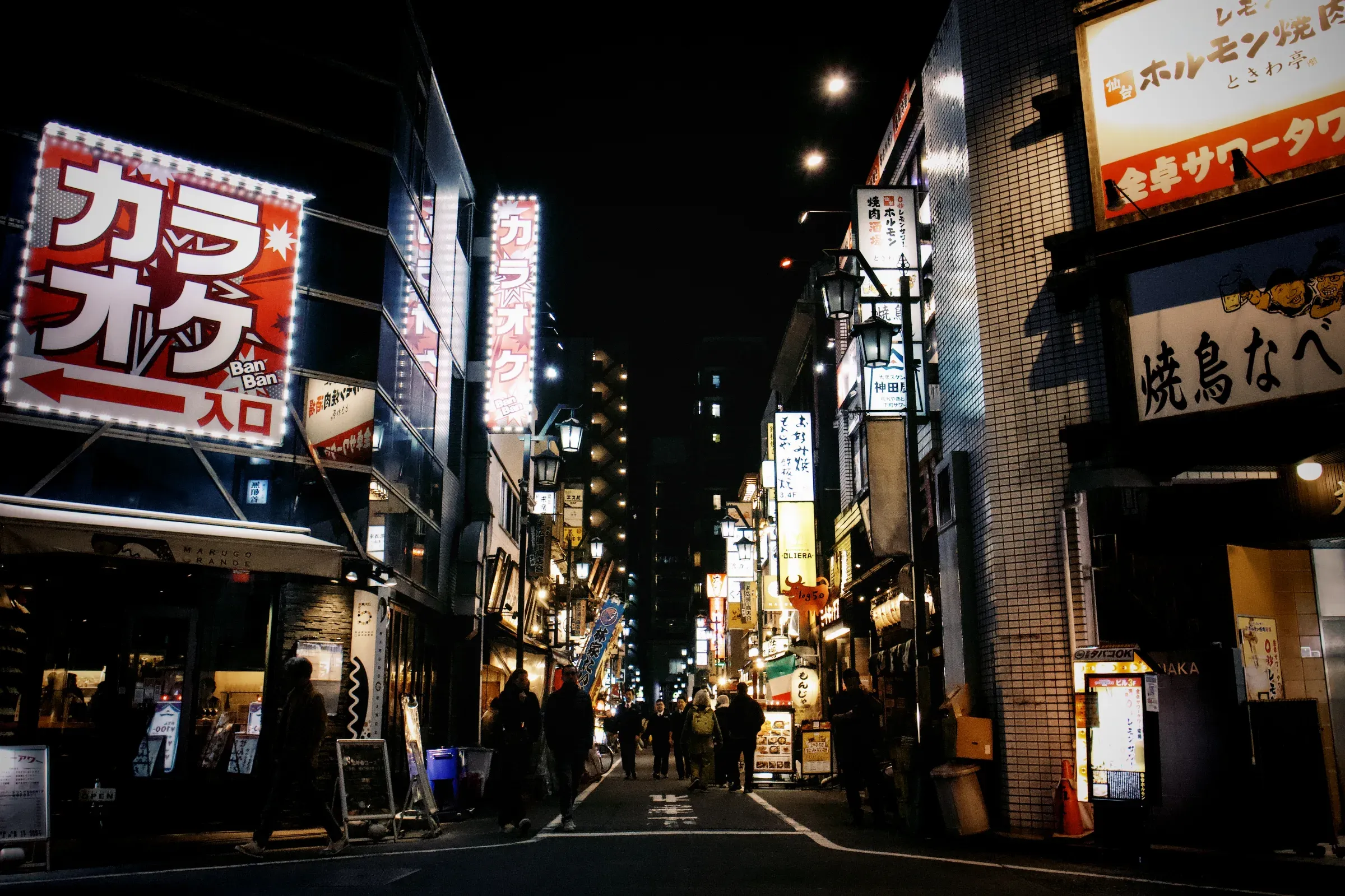 Via di Shinjuku a Tokyo di notte, illuminata da insegne giapponesi e luci di locali lungo la strada.